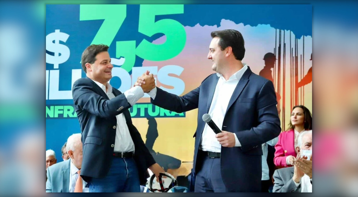 Sandro Alex e o governador Ratinho Junior sorriem e se cumprimentam com um aperto de mão durante evento institucional no Paraná.