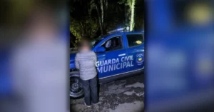 Viatura azul da GCM de Apucarana estacionada à noite enquanto agentes realizam a detenção de mulher de costas ligada a mandado por tráfico.