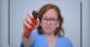 Mulher com o rosto desfocado segurando um spray de pimenta e apontando o dispositivo para o centro da imagem, representando defesa pessoal feminina no Brasil.